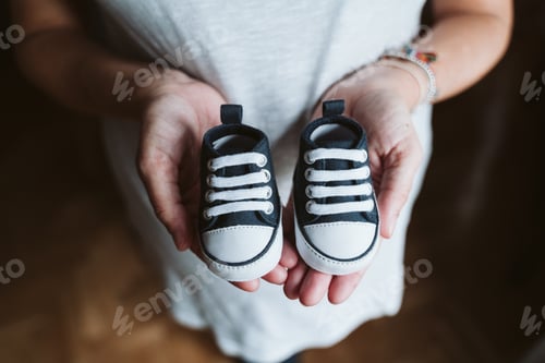 Preview: young pregnant woman at home holding baby shoes