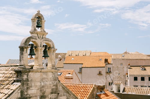 Preview: Three bells on an old stone bell tower among the tiled roofs of city buildings