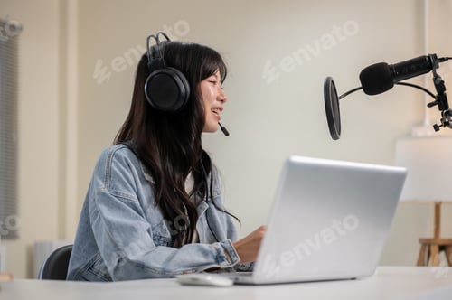 Preview: Asian woman talking hosting a radio or podcast through laptop with headset and mic at home or studio