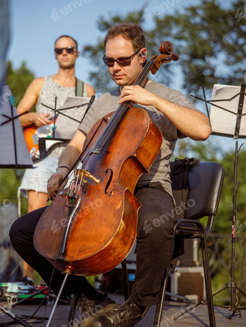 Preview: Male violoncellist playing cello in orchestra outdoors