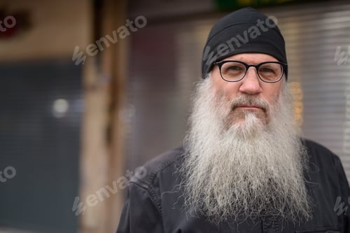 Preview: Face of mature handsome bearded man with eyeglasses in the streets outdoors