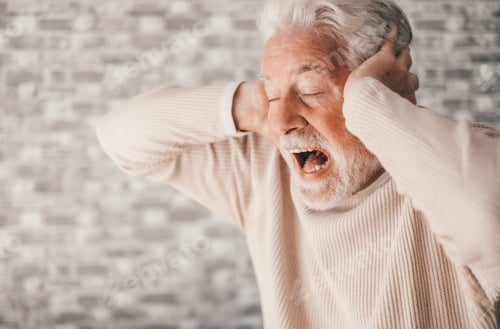 Preview: Desperate frustrated senior man screaming in pain with hands on ears, sitting at home alone