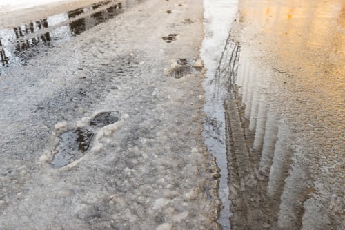 Preview: Footprints in melting snow during thaw at winter day, building with columns in reflection in puddle