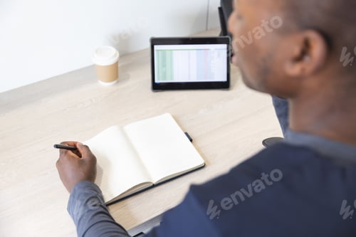 Preview: African american male doctor talking on smartphone and taking notes at reception desk in hospital