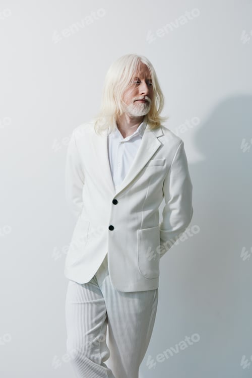 Preview: Elegant senior man in all white attire standing against a light background, exuding confidence and