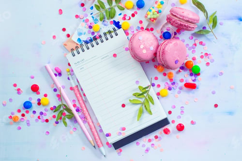 Preview: Open notepad with blank pages in an organizing a party concept with confetti, pink macarons, candies