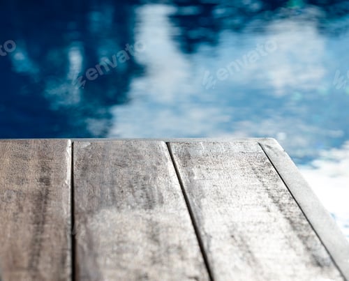 Preview: Empty wooden tabletop in front of a swimming pool with blue water close up and blur. Co