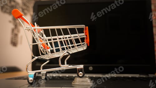 Preview: Miniature shopping cart and a coins on a laptop
