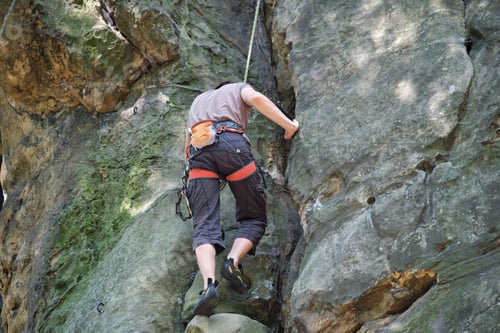 Preview: Determined climber clambering up steep wall of rocky mountain.