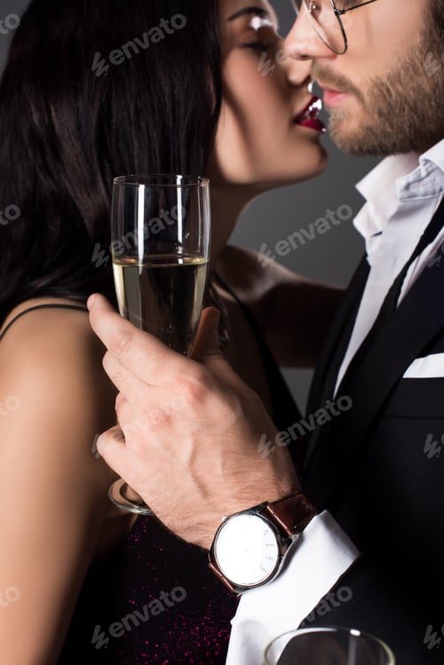 Preview: cropped view of couple holding glass of champagne and going to kiss on valentines day, isolated on