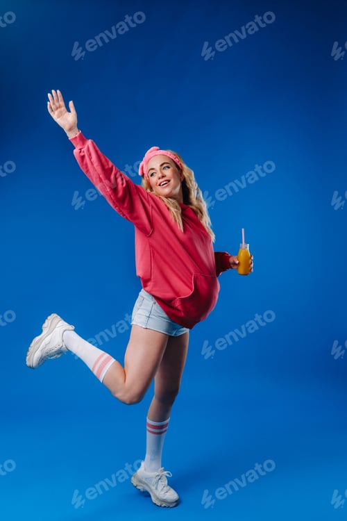 Preview: pregnant girl in pink clothes with a bottle of juice on a blue background
