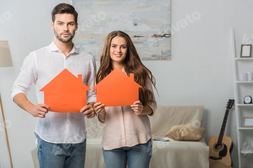 Preview: portrait of smiling couple showing paper houses in hands at new home