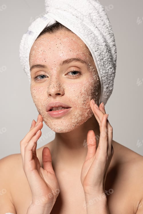 Preview: attractive young woman with towel on head applying coconut scrub on face, isolated on grey