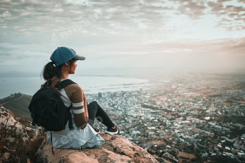 Preview: Young woman sitting on mountain top overlooking city at sunrise