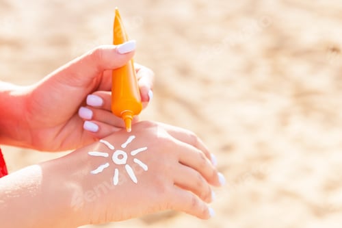 Preview: Young woman is applying sun cream on her hand in sun shape at the beach
