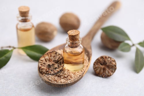 Preview: Nutmeg essential oil and spoon with ground nuts on light table, closeup