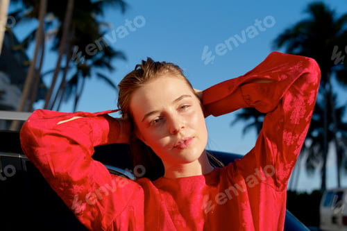 Preview: Woman in a red shirt poses outdoors with palms and blue sky in the background. Miami, FL, USA