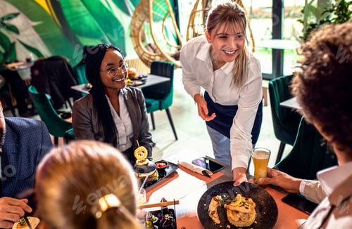 Preview: Smiling waitress serving meal to group of business people in restaurant.