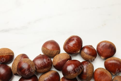 Preview: Sweet fresh edible chestnuts on white marble table, top view. Space for text