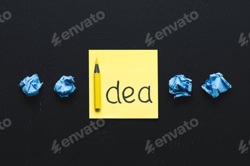 Preview: 'idea' word written on sticky note and blue crumpled paper balls on black background, ideas concept