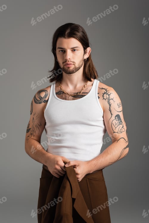 Preview: Tattooed long haired man holding jacket standing isolated on grey