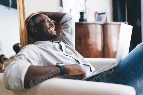 Preview: Laughing black man sitting with laptop on sofa