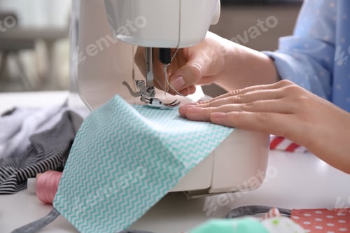 Preview: Woman making cloth mask with sewing machine at white table, closeup