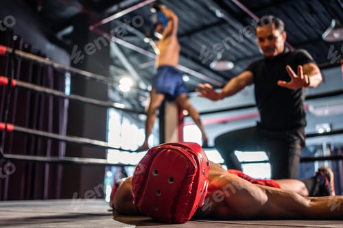 Preview: Boxing referee check fallen competitor after knockout on stage.