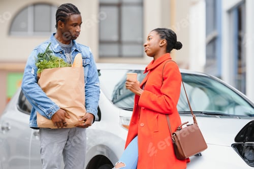 Preview: Happy young adult african american man and smiling woman charging electric car.