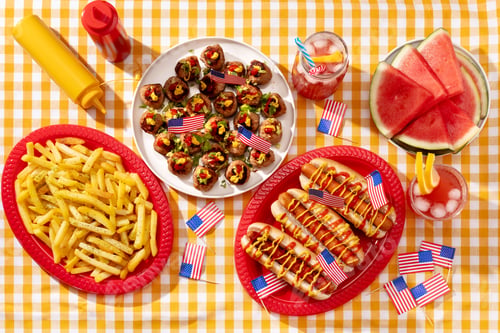 Preview: American food on a checkered yellow table with hot dogs, fries, meatballs, decorated with USA flags.