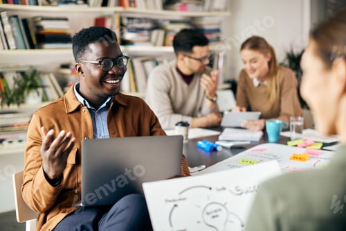 Preview: Happy African American businessman using laptop while talking to colleague at creative office.