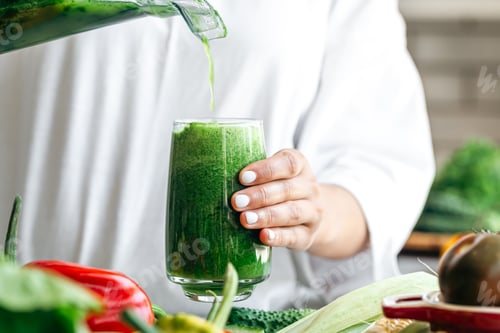 Preview: A woman pouring green smoothie to glass, healthy food concept.