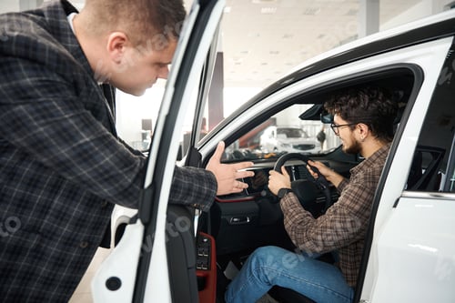 Preview: Man buying new automobile in showroom talking with manager about car models