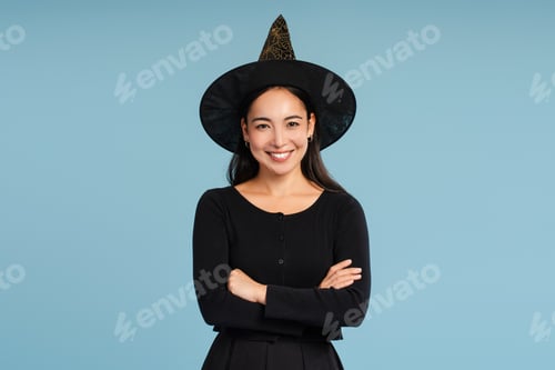 Preview: Happy Asian woman wearing witch hat smiling with crossed arms looking at camera on blue background