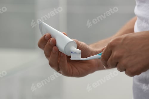 Preview: Man applying toothpaste on brush in bathroom, closeup