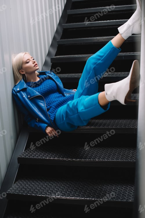 Preview: blonde woman wearing blue leather jacket and heels sitting on stairs