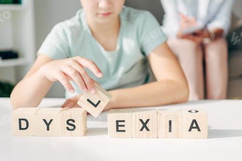 Preview: cropped view of kid with dyslexia sitting at table and playing with wooden cubes