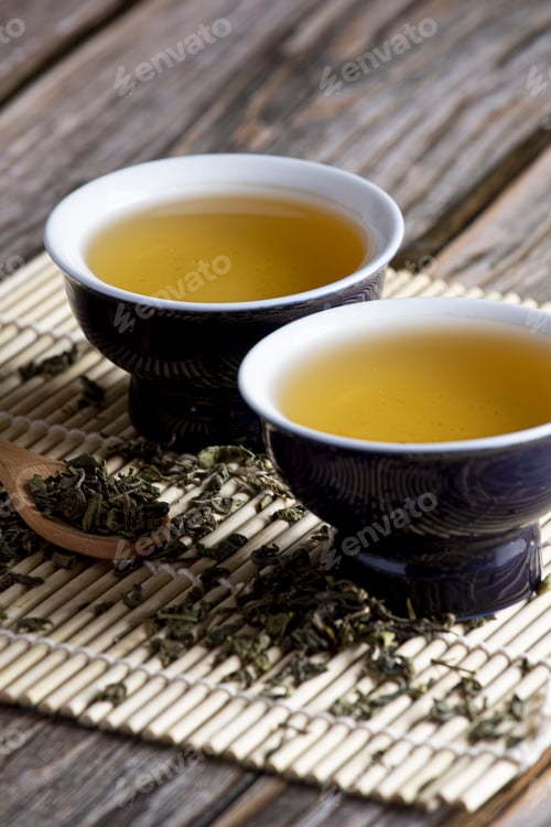 Preview: Vertical selective focus shot of green leaf tea and two containers on wooden background
