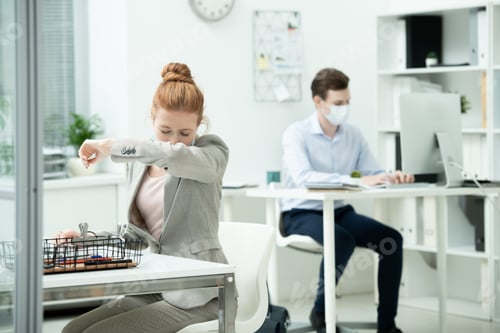 Preview: Young female office manager in suit and protective mask going to sneeze