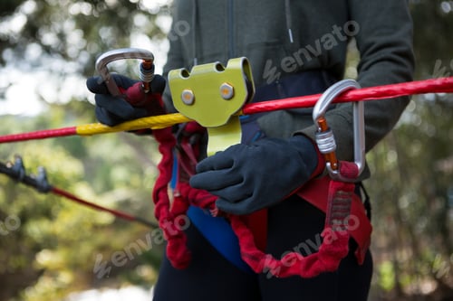 Preview: Woman adjusting her harness on zip line cable in the forest on a sunny day