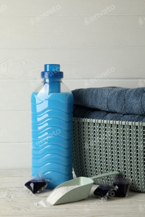 Preview: Basket with towels, laundry capsules, scoop with powder and detergent on wooden background