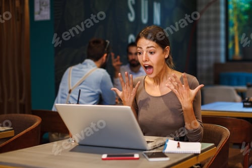 Preview: Excited young woman using a laptop in a cafe