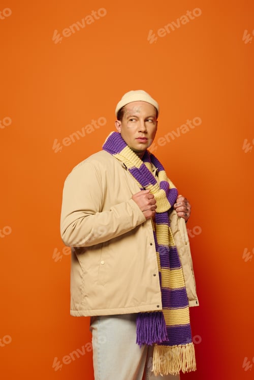 Preview: A young man with tattoos poses fashionably in a colorful scarf against an orange backdrop