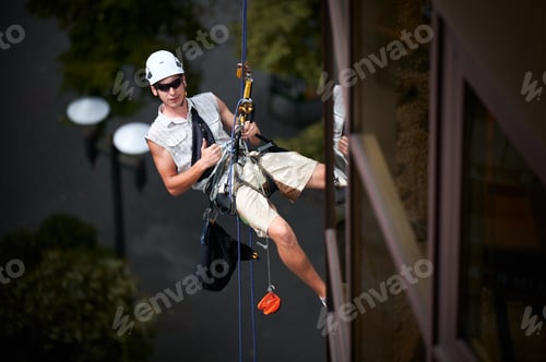 Preview: Industrial mountaineering worker cleaning window outside building.