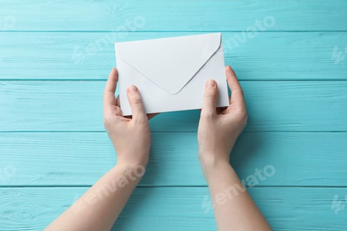 Preview: Woman with white paper envelope at light blue wooden table, top view