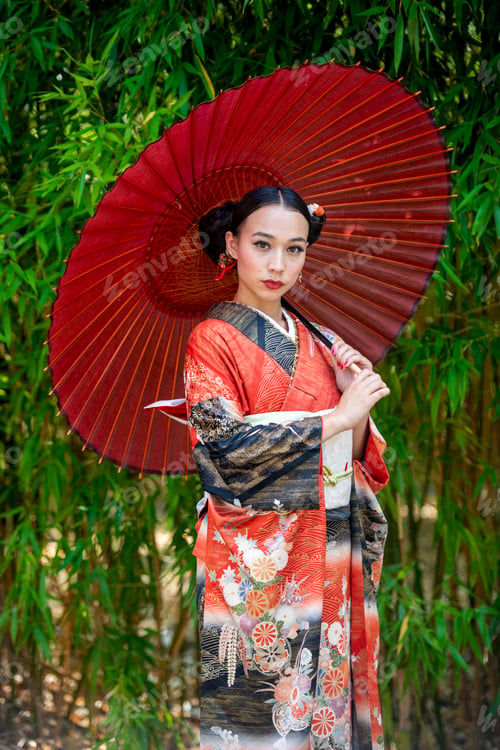 Preview: Elegant woman in traditional kimono with a red parasol standing amidst lush greenery