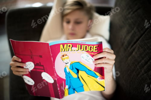 Preview: Young caucasian man lying on the couch reading cartoon