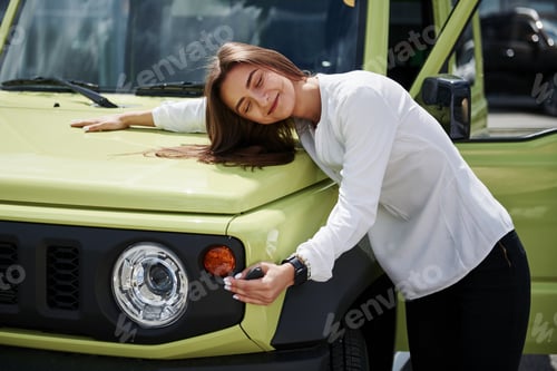 Preview: Keys in hand. Young woman in white official clothes stands in front of green automobile outdoors