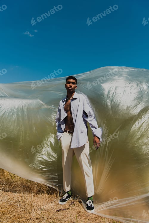 Preview: full length of african american man in summer outfit standing in meadow near polyethylene film