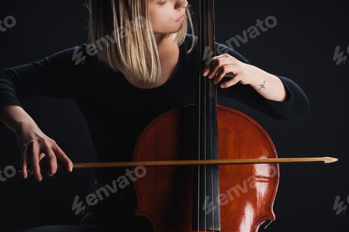 Preview: partial view of tattooed woman playing double bass in darkness isolated on black